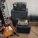 Elektrická kytara s trupem v barevném přechodu od žluté po červenou a bílým pickguardem. Na hlavě kytary je nápis Gibson a La Paul. Vedle ní stojí če…