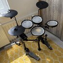 Elektronická bicí souprava černé barvy s bílými membránami. Na modulech a rámu je viditelný nápis Roland a na membránách označení V-Drums. Souprava o…