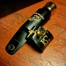 Černý munční nástroj (mouthpiece) s kovovou zlatou zátkou. Na povrchu je zlatý nápis „Jody Jazz CUSTOM DARK“ a označení „T-5*“. Součástí je černý kož…