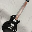 Černá elektrická kytara s tmavě hnědým hmatníkem a dvěma humbuckery s bílými plastovými krytkami. Na hlavě je bílý nápis Epiphone a zlaté logo s podp…