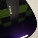 Detailní pohled na Rounded povrch hudebního přístroje s tmavě fialovým metalizovaným lakem. Na povrchu je vidět řada šesti malých kulatých kontrolníc…