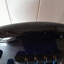 Detailní pohled na černý, lesklý povrch těla hudebního nástroje. Povrch je v horní části posetý drobnými nečistotami a prachem. Ve spodní části jsou…