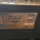 Detail stříbrného kovového štítku na černém povrchu kytarového komba. Na štítku je uveden název modelu Hot ROD Deluxe a nápis A PRODUCT OF: FENDER MU…