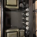 Fotografie zachycuje vnitřek černého elektronického zařízení, pravděpodobně zesilovače. Vevnitř jsou umístěny čtyři elektronky a tři kovové transform…