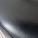 Detailní záběr na černý povrch z materiálu imitující kůži s výraznou strukturou. Na okraji je viditelný červený steh. Povrch vykazuje drobné nečistot…
