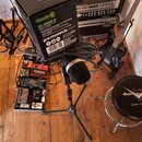 Fotografie zachycuje mikrofon na stativu, na kterém je umístěna černá krabice s nápisy Gravity, MA DRINK M a gravitystands.com. Vedle stativu se nach…