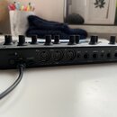 Zadní strana černého elektronického hudebního zařízení s několika ovládacími knoflíky na horní ploše. Jsou zde viditelné nápisy: microSD, Thru, Out,…