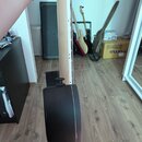 Detailní pohled na hmatník a krk elektrické kytary s černým trupem. Na hmatníku jsou vidět kovové pražce a jedna struna. V pozadí jsou vidět další ky…