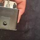 Fotografie zachycuje detail spodní části černého kytarového efektu. V centru je vidět vstupní nebo výstupní konektor typu jack. Na zařízení nejsou žá…