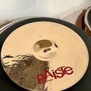 Kruhový mosazný činel s jemným žebrováním povrchu. Na spodní části je červený nápis pAiste a pod ním menší bílý text MADE IN SWITZERLAND. V horní čás…