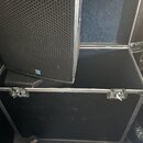 Černý reproduktor s voštinovou mřížkou je umístěn v otevřeném transportním kufru. Kufr má černý povrch, hliníkové hrany a dvě kovové zavírací zámky.…