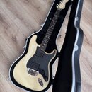 Elektrická kytara krémové barvy s černým pickguardem v černém tvrdém kufru. Na hlavě hmatníku je viditelné logo "Fender". Nástroj má dva snímače typu…