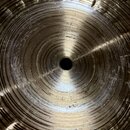 Detailní pohled na spodní stranu kovového činele zlatavé barvy. Povrch vykazuje koncentrické drážky a v horní části jsou vidět hlubší rýhy a známky o…