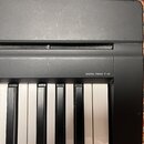 Detailní pohled na část klávesnice digitálního piana v černé barvě. Na horní liště je bílý nápis DIGITAL PIANO P-45. Povrch plastového šasi vykazuje…