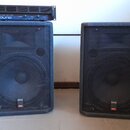 Dva černé reproduktorové boxy s kovovými ochrannými mřížkami. Na spodní části obou boxů je malý štítek s nápisy „SOUND SYSTEM“ a „PROEL“. Na levém re…