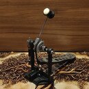 Černý pedál basového bubnu s kovovými mechanismy a stříbrnou tyčí beateru. Na horním kole je bílý nápis POWER GLIDE. Povrch pedálu je černý, s několi…