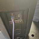 Detail zadní strany černého aktivního reproduktoru. Na ovládacím panelu jsou vidět kontrolky LIMITER, SIGNAL a POWER, přepínače FLAT/BOOST a LINE/MIC…