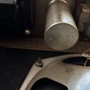 Detailní pohled na vnitřní komponenty elektronického zařízení. Je vidět kovový válcový kondenzátor a část šasi s pájenými spoji. Na černém povrchu vl…