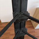 Fotografie zachycuje detail černé kovové konstrukce stojanu. Jsou vidět dvě úrovně s rozkládacími rameny a plastovými spojovacími prvky. Povrch vykaz…