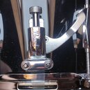 Detailní záběr na černý kotel bubnu s chromovaným obručováním. Na boku je připevněn chromovaný mechanismus s nápisem Pearl. Povrch nástroje je glossy…