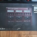 Fotografie znázorňuje kartonovou krabici s obrázkem červeného efektového procesoru. Na krabici jsou nápisy ZOOM B3n Multi-Effects Processor a v dolní…