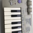 Detailní pohled na ovládací panel a klávesy šedého MIDI kontroléru. Na panelu jsou tlačítka s nápisy OCTAVE RESET, OCTAVE SHIFT a SHIFT, dvě červené…