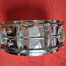 Stříbrný, chromovaný snare drum z kovu s vysokým leskem. Na koruse jsou vidět napínací šrouby a úchytky. Povrch je čistý a bez viditelného opotřebení…