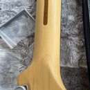 Detail zadní strany krku kytary zCvětlého dřeva s tmavým středovým pruhem. V dolní části je vidět chromovaný ladicí kolík. Povrch dřeva je hladký a b…