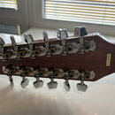 Zadní strana hmatníku s ladicími kolíky u twelve-string kytary z tmavého dřeva. Na zadní straně hlavy je nalepený žlutý štítek s nápisem MADE IN KORE…