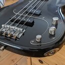 Detailní pohled na spodní část černého elektrického basového kytary s lesklým povrchem. Nástroj má chromovaný kobylník, tři chromované oválné knofíky…
