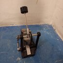 Fotografie znázorňuje basový pedál s řetězovým pohonem v černé barvě. Na horní části mechanismu je viditelný nápis "TAMA". Nástroj vykazuje známky bě…