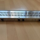 Stříbrné kovové zařízení v rackovém provedení s ventilační mřížkou na horní straně. Na předním panelu jsou umístěny čtyři konektory XLR. Povrch vykaz…