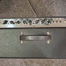Horní pohled na kytarový zesilovač v černém texturovaném potahu. Stříbrný ovládací panel obsahuje nápisy INPUTS, VOLUME, DRIVE, TREBLE, BASS, MIDDLE,…