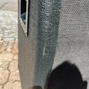Detailní pohled na roh černého reproduktoru nebo komba. Je vidět povrch z texturovaného vinylu a část přední textilní masky. V horní části je vidět k…