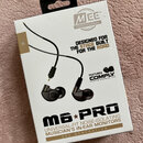 Fotografie znázorňuje krabici s in-ear monitory. Na obalu je nápis Mee PROFESSIONAL, text DESIGNED FOR THE STAGE BUILT FOR THE ROAD a FEATURES COMPLY…