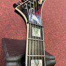 Detail krku a hlavy elektrické kytary v černé barvě s bílým lemováním. Na hlavě je viditelné logo Gibson. Hmatník je tmavý s dvěma čtvercovými perleť…