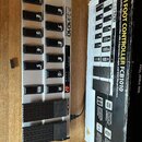 Stříbrný MIDI kontrolér s černými spínači a dvěma expresními pedály. Na přístroji je nápis FCB1010 MIDI FOOT CONTROLLER a na pedálech logo Behringer.…