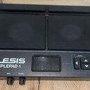 Černý elektronický samplepad s dvěma velkými gumovými pady. Na přístroji je bílý nápis ALESIS SAMPLEPAD 4 a v pravé části ovládací prvky s popisky OP…