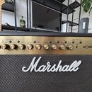 Kytarový kombozesilovač značky Marshall s černým potahem a zlatým ovládacím panelem. Na mřížce reproduktoru je bílé logo Marshall a vpravo na panelu…
