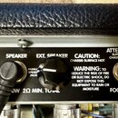 Detail zadní strany zesilovače s černým panelem a texty v bílé barvě. Jsou zde vidět nápisy SPEAKER, EXT. SPEAKER, CAUTION: CHASSIS SURFACE HOT a ATT…