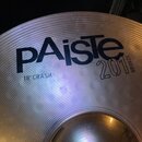 Detailní pohled na kovový činel v zlatavé barvě s koncentrickým žebrováním povrchu. Na povrchu je černý nápis pAiste a vedle něj nápis 20i BRONZE. Po…
