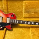 Elektrická kytara s červeno-žlutým sunburst povrchem těla a hnědým hmatníkem s bílými blokovými vložkami. Na hlavě je viditelné logo Epiphone a nápis…