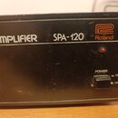 Černý zesilovač s nápisy ER AMPLIFIER a SPA-120. V pravé horní části je oranžové logo Roland. Zařízení má červenou kontrolku a vypínač s označením PO…