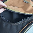 Detail otevřené kapsy na černé a hnědé brašně z textilního materiálu. Na hnědém povrchu je vidět část nápisu RITTER a malý štítek s nečitelným označe…