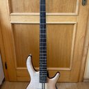 Elektrická basová kytara s přírodním dřevěným povrchem těla a hmatníkem z tmavého dřeva. Na hlavě je viditelné logo "Ibanez". Nástroj má dva humbucke…