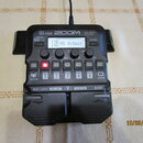 Černý multi-efektový procesor s nápisy G1 FOUR a ZOOM Multi-Effects Processor. Displej zobrazuje text 10 MS HiGain. Zařízení obsahuje čtyři ovládací…