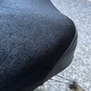 Detailní záběr na roh černé polstrované sedací plochy. Povrch je potažen černým textilem s jemnou strukturou a zakončen hladkým černým okrajem. Žádné…