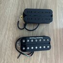 Dva elektrické kytarové snímače typu humbucker v černé barvě. Horní snímač má černé plastové krytky s viditelnými poloslnoidy. Dolní snímač má stříbr…
