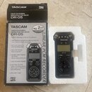 Na fotografii je černý digitální záznamník TASCAM DR-05 v originálním kartonovém obalu a bílém polystyrenovém podkladu. Na přístroji i na krabici jso…