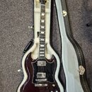 Tmavě vínová elektrická kytara s černým pickguardem v tvrdém kufru s bílou výplní. Na hlavě hmatníku je zlatý nápis Gibson. Kytara má dva humbuckery,…